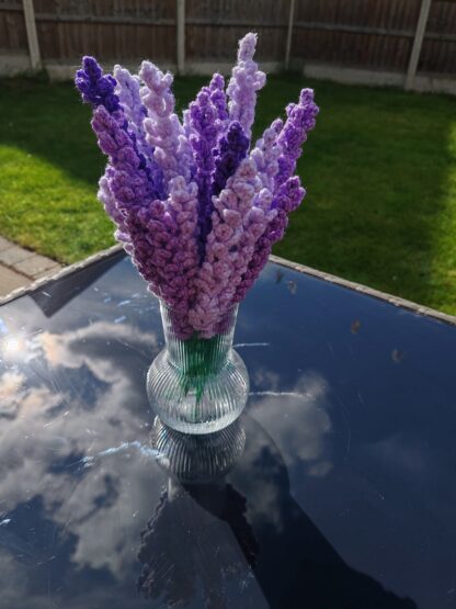 Bunch of hand made lavender sprigs in a vase, on a table outside.