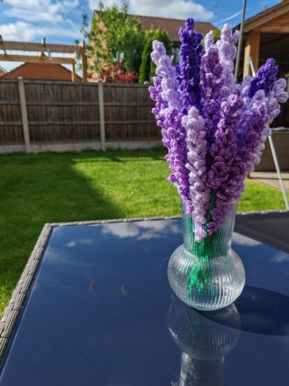 Bunch of hand made lavender sprigs in a vase, on a table outside.